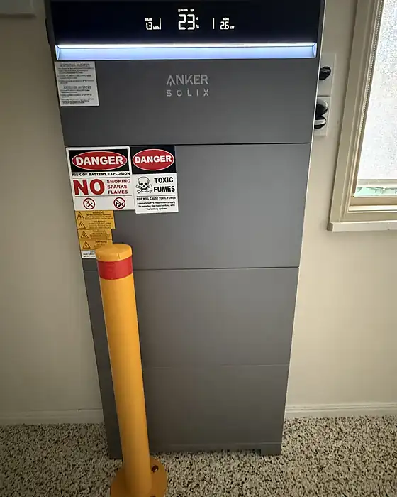 A tall Anker Solix home battery installed indoors with bollard protection and safety signage