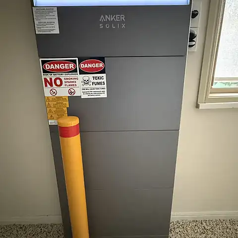 A tall Anker Solix home battery installed indoors with bollard protection and safety signage