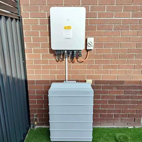 A wall-mounted hybrid inverter above a stacked home battery on a brick wall