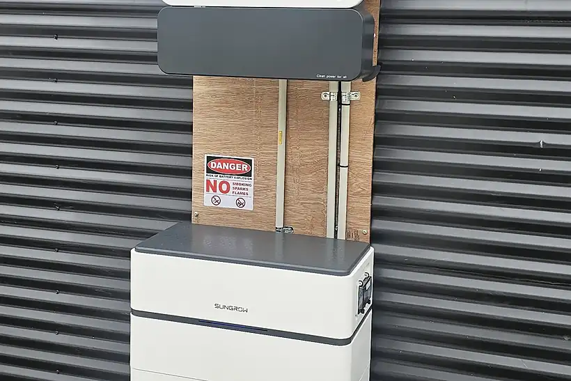 A tall inverter over a stacked white battery on a dark corrugated wall