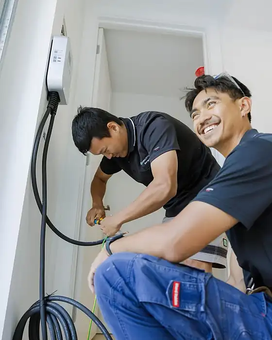 Two LMS electricians in navy polos wiring up an EV charger, one smiling