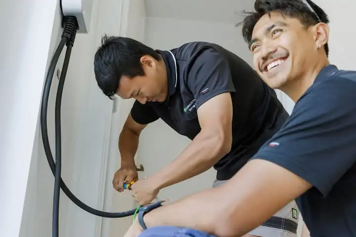 Two LMS electricians in navy polos wiring up an EV charger, one smiling