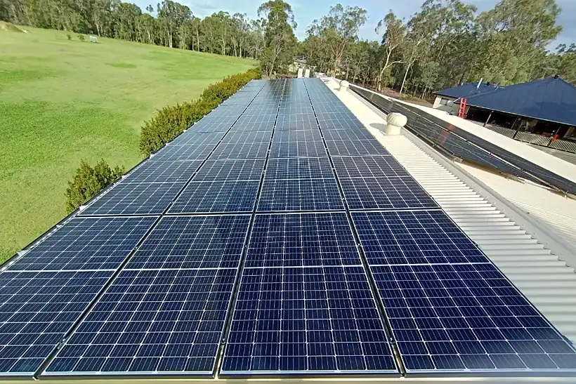 Close view of blue solar panels on a corrugated shed roof with green paddocks beyond