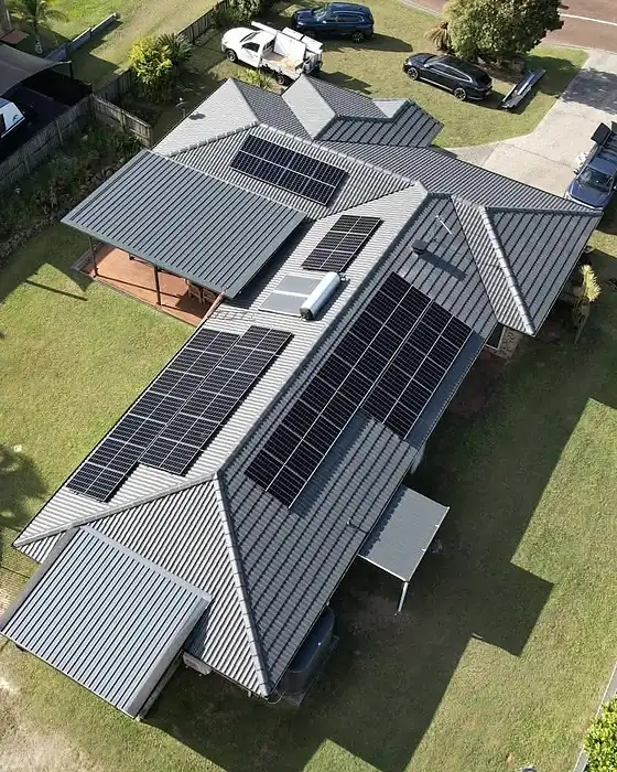 Drone view of a grey metal roof home with two solar arrays and a green backyard
