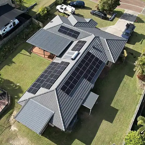 Drone view of a grey metal roof home with two solar arrays and a green backyard