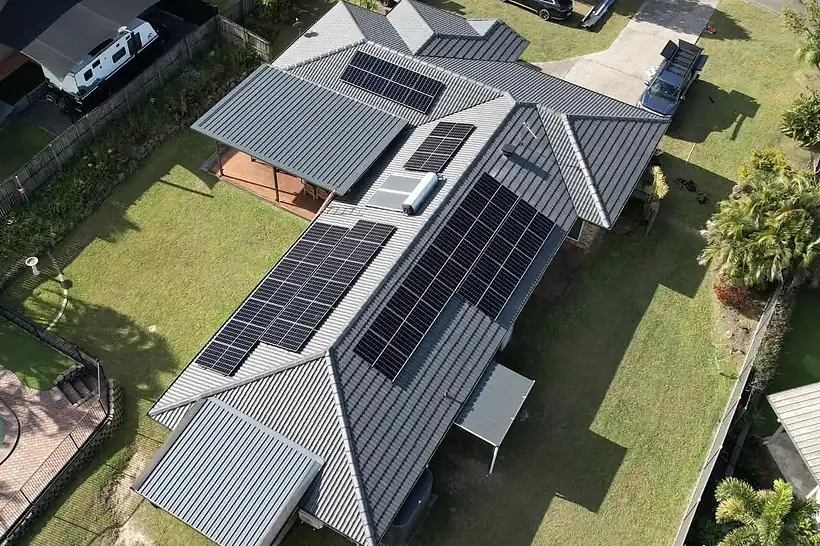 Drone view of a grey metal roof home with two solar arrays and a green backyard