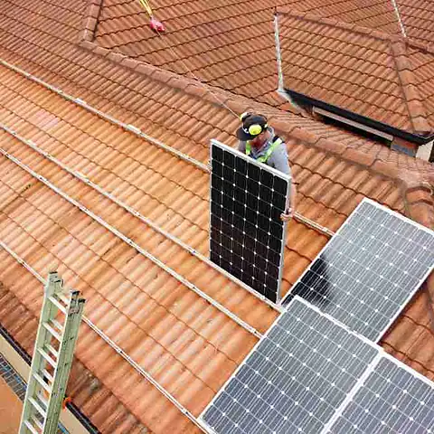 Aerial view of a terracotta roof with an installer lifting a panel off its rails before a roof restoration