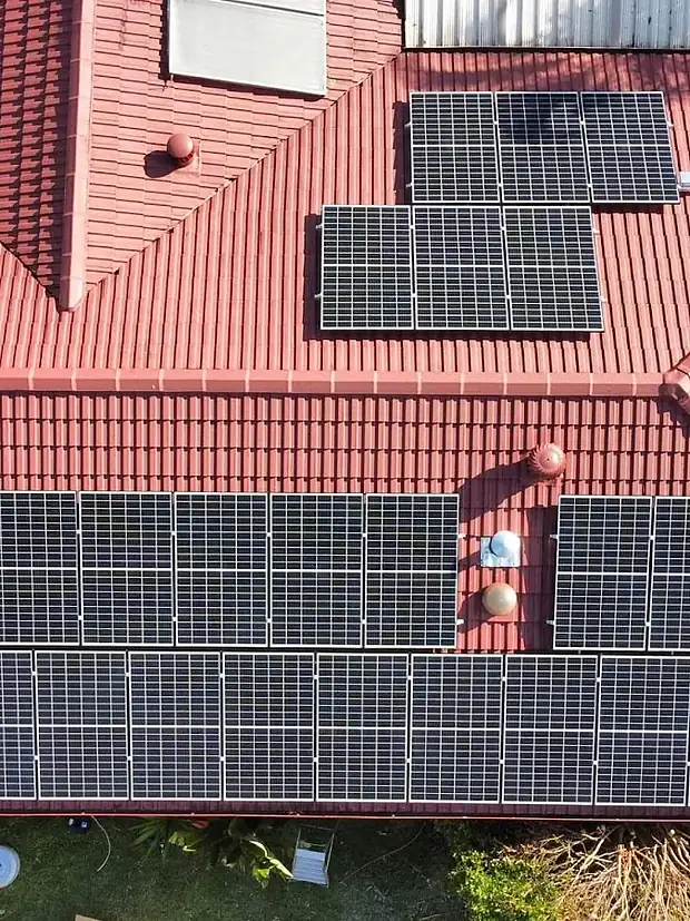 Aerial view of a red tiled house roof in South East Queensland with several rows of black solar panels installed by LMS Electrical