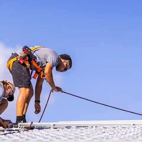 Two LMS Electrical installers in safety harnesses working on a metal roof
