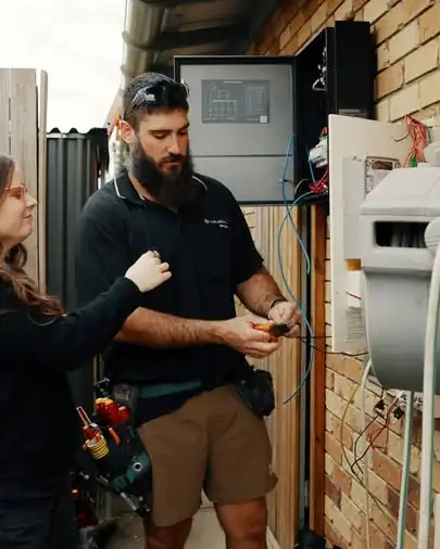 An LMS electrician working at a switchboard on the side of a brick house