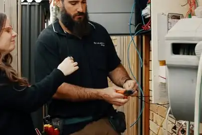 An LMS electrician working at a switchboard on the side of a brick house